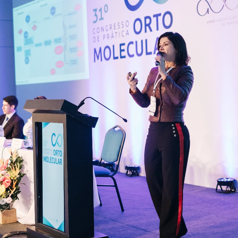 Claudia Guimarães palestrando no Congresso de Prática Ortomolecular, com outros profissionais de saúde ao fundo